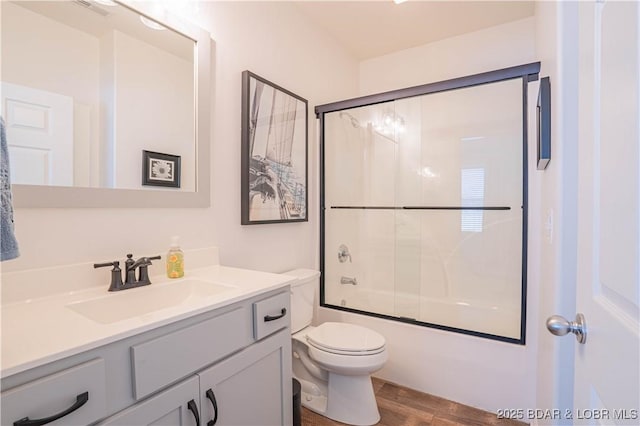 bathroom featuring visible vents, toilet, wood finished floors, combined bath / shower with glass door, and vanity