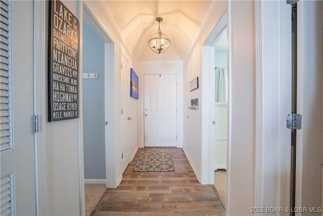 hall featuring a notable chandelier, baseboards, and wood finished floors