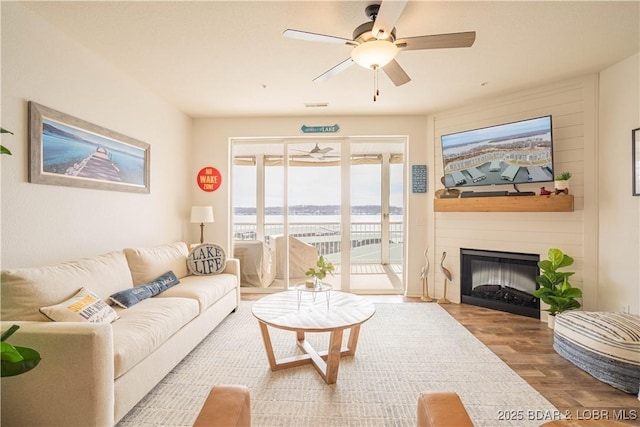 living room with a ceiling fan, visible vents, a fireplace, and wood finished floors