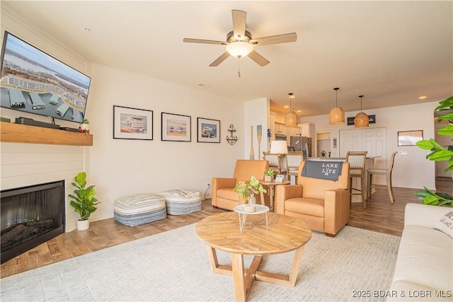 living room with a ceiling fan, light wood-type flooring, and a fireplace