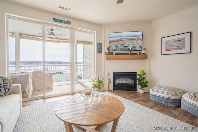 living room featuring a fireplace, visible vents, a ceiling fan, and wood finished floors