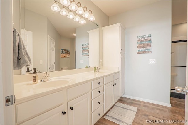 bathroom featuring toilet, double vanity, a sink, and wood finished floors