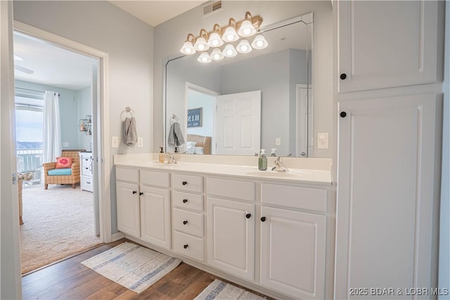 ensuite bathroom with double vanity, visible vents, connected bathroom, a sink, and wood finished floors