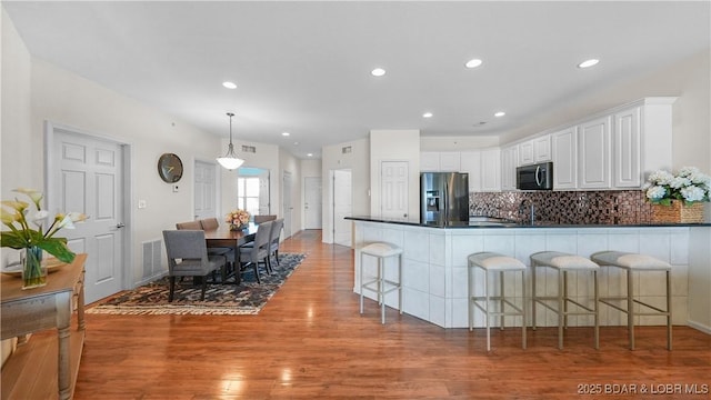 kitchen featuring dark countertops, decorative backsplash, light wood-style floors, stainless steel fridge, and a peninsula