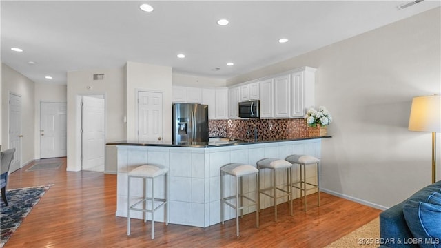 kitchen featuring tasteful backsplash, dark countertops, stainless steel refrigerator with ice dispenser, and wood finished floors