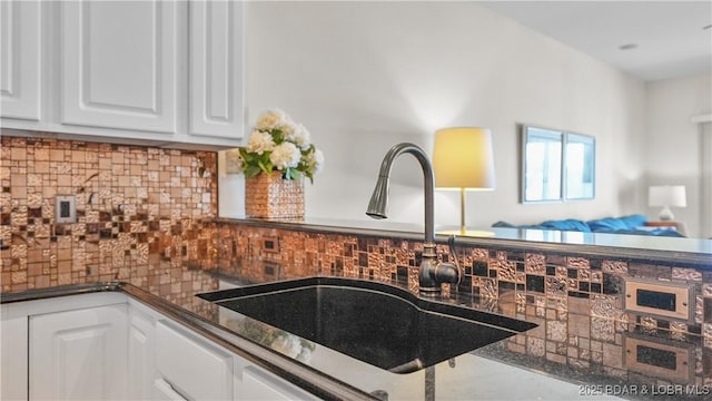 interior details featuring backsplash, dark countertops, a sink, and white cabinetry