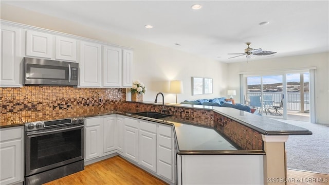 kitchen featuring a peninsula, a sink, open floor plan, appliances with stainless steel finishes, and tasteful backsplash