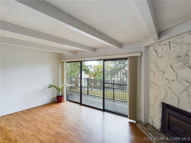 spare room with a textured ceiling, a fireplace, wood finished floors, baseboards, and beam ceiling