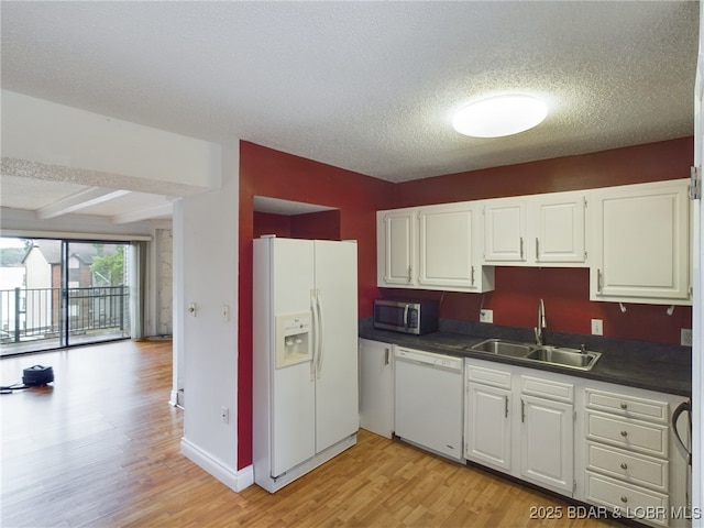 kitchen featuring light wood finished floors, dark countertops, white cabinets, a sink, and white appliances