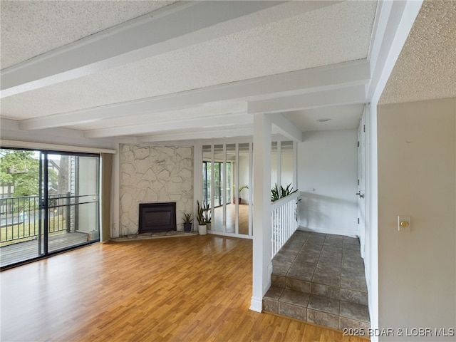 unfurnished living room featuring a textured ceiling, a glass covered fireplace, wood finished floors, and beam ceiling