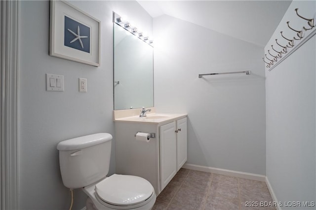 bathroom with toilet, vanity, baseboards, vaulted ceiling, and tile patterned floors