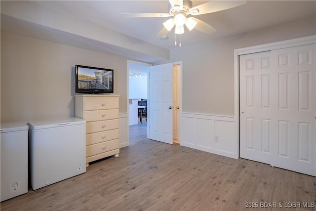 unfurnished bedroom with fridge, light wood finished floors, a closet, and wainscoting