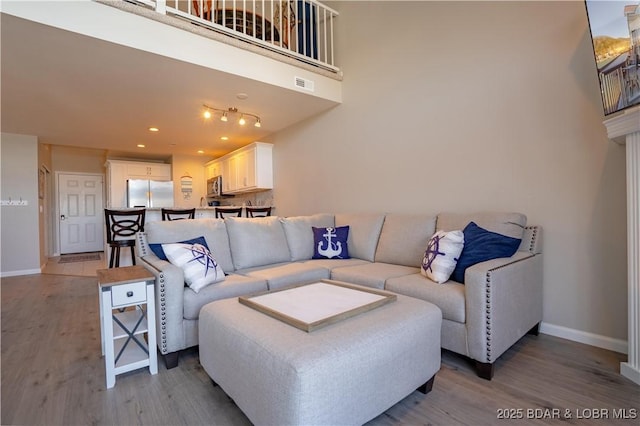 living area with light wood finished floors, visible vents, baseboards, a high ceiling, and recessed lighting