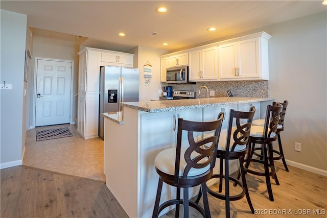 kitchen with tasteful backsplash, white cabinets, appliances with stainless steel finishes, light stone counters, and a peninsula