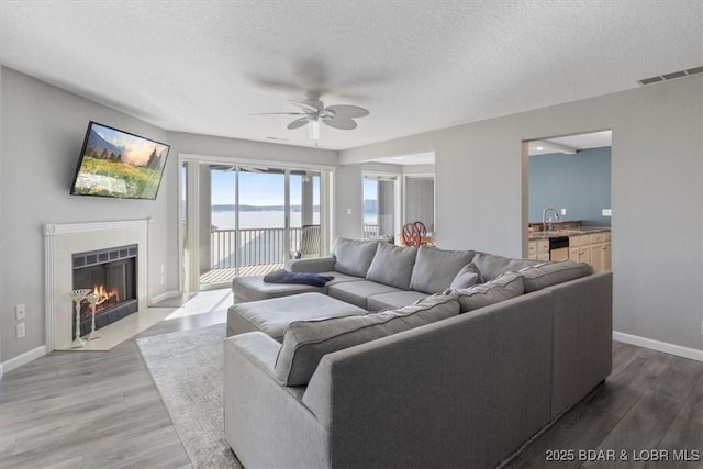 living room with a fireplace with flush hearth, a ceiling fan, a textured ceiling, wood finished floors, and baseboards