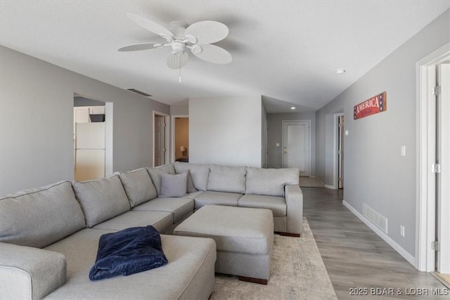 living area with light wood-style flooring, visible vents, ceiling fan, and baseboards