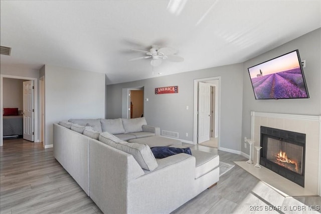 living area featuring a ceiling fan, visible vents, baseboards, light wood-type flooring, and a tiled fireplace