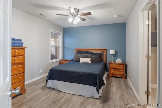 bedroom featuring visible vents, a textured ceiling, baseboards, and wood finished floors