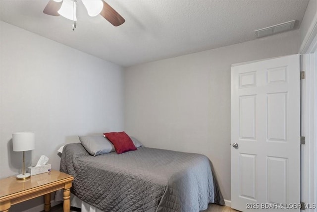 bedroom with a textured ceiling, visible vents, and a ceiling fan