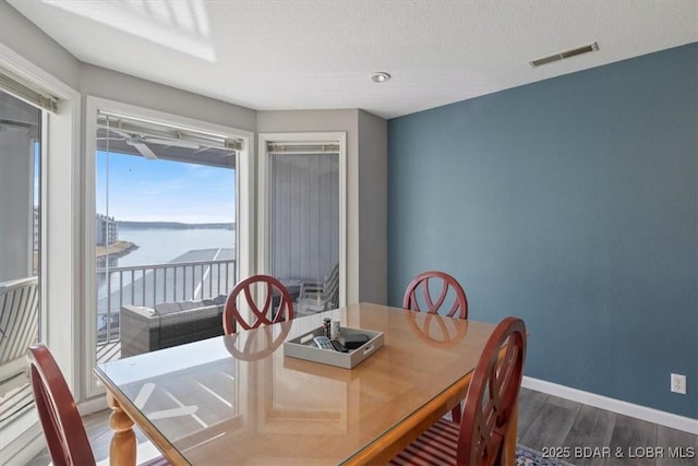 dining room with visible vents, a water view, a textured ceiling, wood finished floors, and baseboards