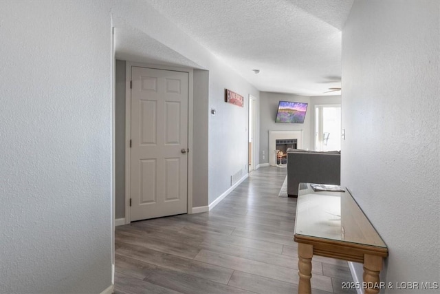 corridor with visible vents, baseboards, a textured wall, wood finished floors, and a textured ceiling