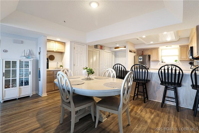 dining area with dark wood-style floors, a raised ceiling, and recessed lighting