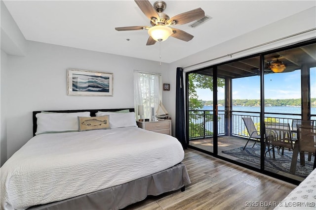 bedroom featuring access to outside, multiple windows, a water view, and wood finished floors