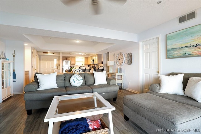 living area featuring a tray ceiling, dark wood-style flooring, visible vents, and baseboards