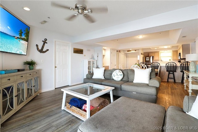 living area with visible vents, baseboards, a raised ceiling, a ceiling fan, and dark wood-style floors