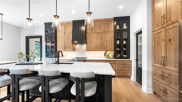 kitchen with decorative backsplash, a kitchen breakfast bar, stainless steel range with electric cooktop, light wood-style floors, and a sink