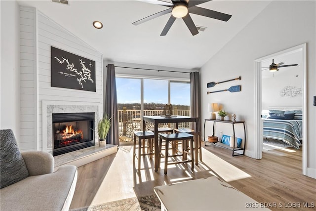 dining area with a premium fireplace, wood finished floors, a ceiling fan, baseboards, and vaulted ceiling