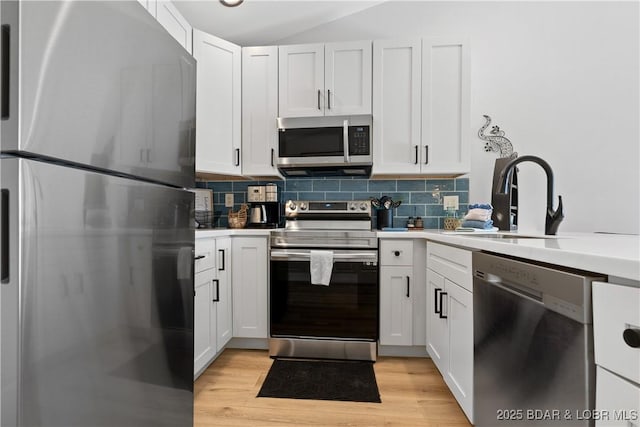 kitchen featuring light wood finished floors, appliances with stainless steel finishes, a sink, and tasteful backsplash