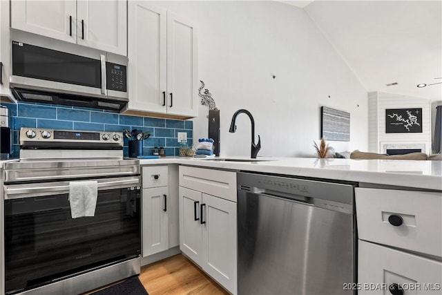 kitchen featuring stainless steel appliances, light countertops, decorative backsplash, vaulted ceiling, and a sink