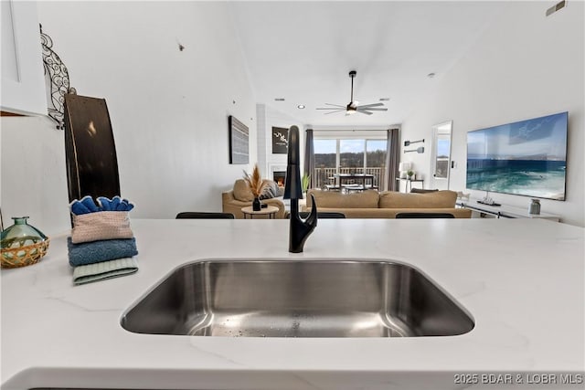 interior details featuring visible vents, ceiling fan, light stone countertops, white cabinetry, and a sink