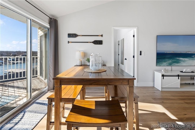 dining area featuring lofted ceiling, a water view, baseboards, and wood finished floors