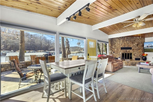 sunroom featuring lofted ceiling with beams, wood ceiling, a ceiling fan, and a stone fireplace