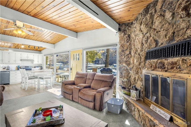 living room featuring vaulted ceiling with beams, a stone fireplace, wooden ceiling, and a ceiling fan