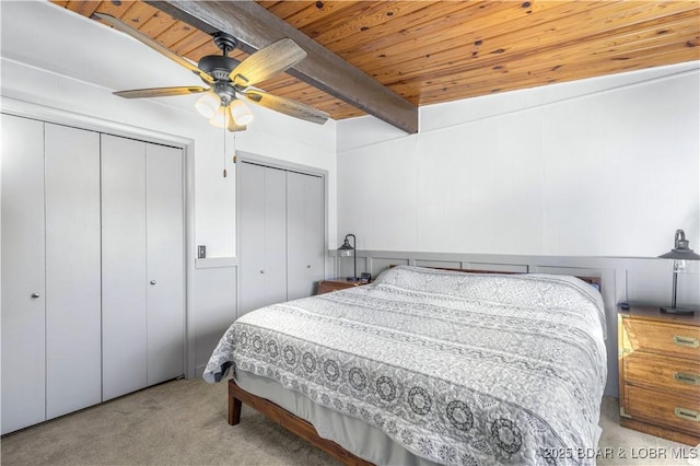 carpeted bedroom with wood ceiling, ceiling fan, multiple closets, and beamed ceiling