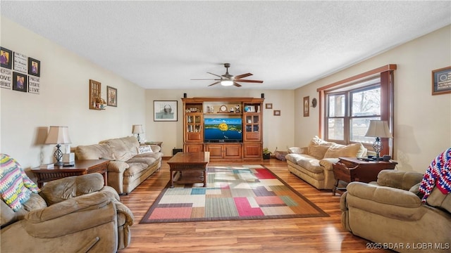 living area with light wood-style flooring, ceiling fan, and a textured ceiling