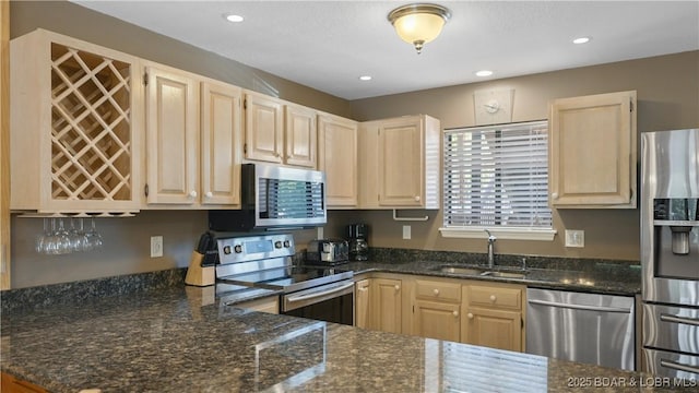 kitchen with stainless steel appliances, dark stone counters, a sink, and light brown cabinetry