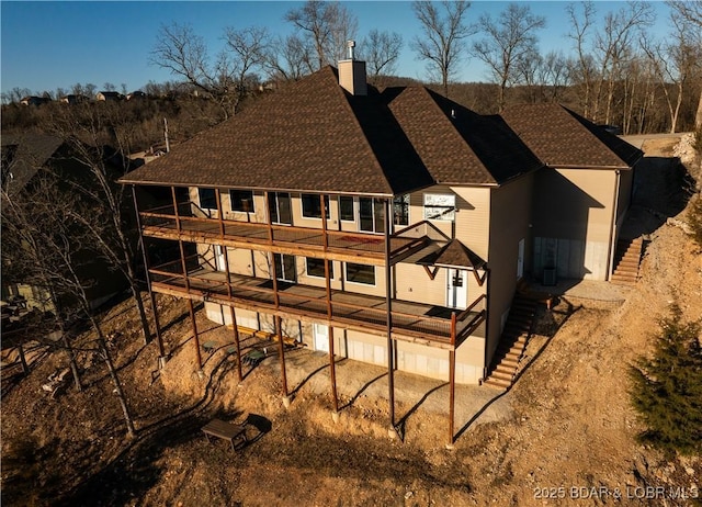 back of house with stairway, a chimney, and a shingled roof