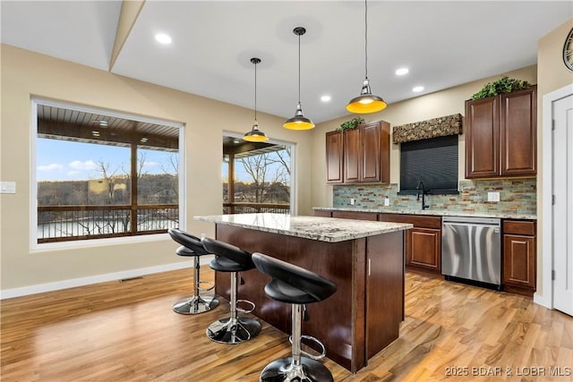 kitchen featuring dishwasher, a kitchen island, a kitchen breakfast bar, light wood-type flooring, and backsplash