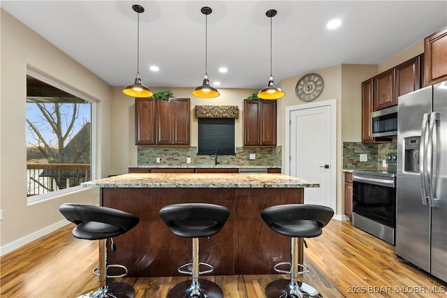 kitchen featuring stainless steel appliances, light wood-type flooring, a center island, and a breakfast bar area