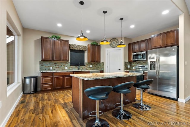 kitchen with a breakfast bar, dark wood-style flooring, a sink, a kitchen island, and appliances with stainless steel finishes