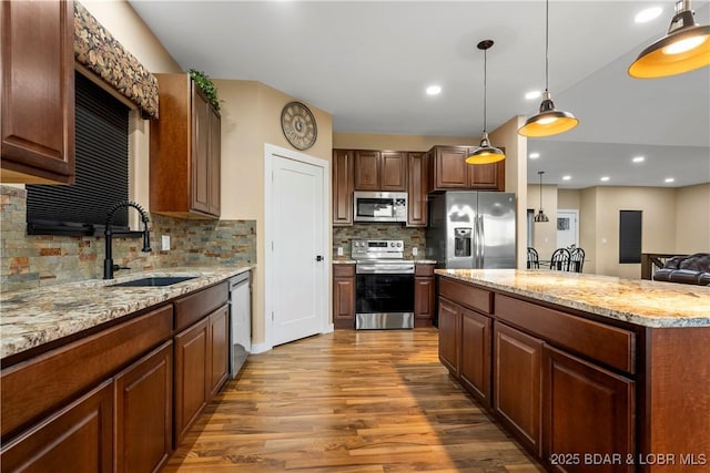 kitchen featuring appliances with stainless steel finishes, wood finished floors, decorative light fixtures, light stone countertops, and a sink