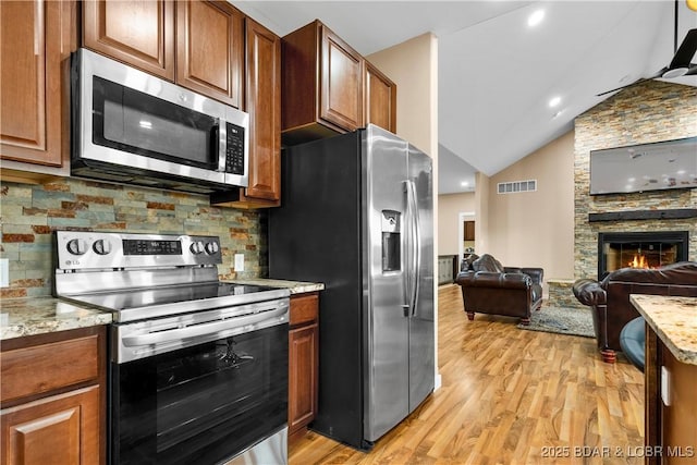 kitchen with visible vents, light wood-style flooring, open floor plan, stainless steel appliances, and a stone fireplace