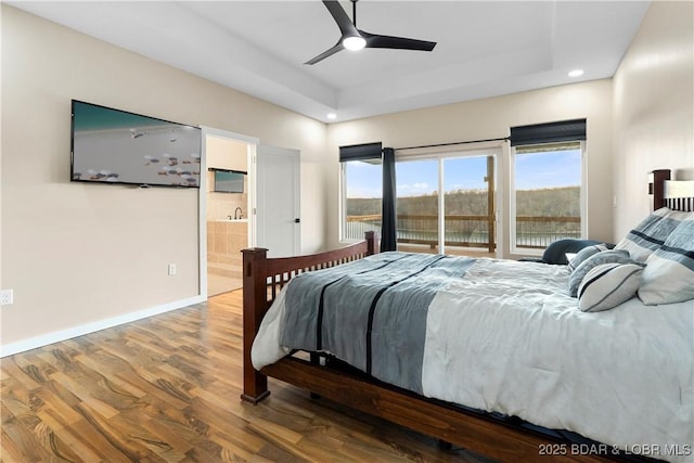 bedroom with connected bathroom, wood finished floors, a ceiling fan, baseboards, and a raised ceiling