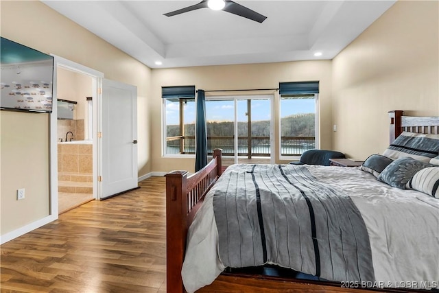 bedroom featuring access to exterior, baseboards, a tray ceiling, and wood finished floors