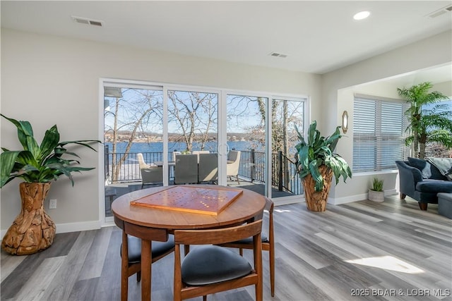 dining space featuring a water view, baseboards, visible vents, and wood finished floors