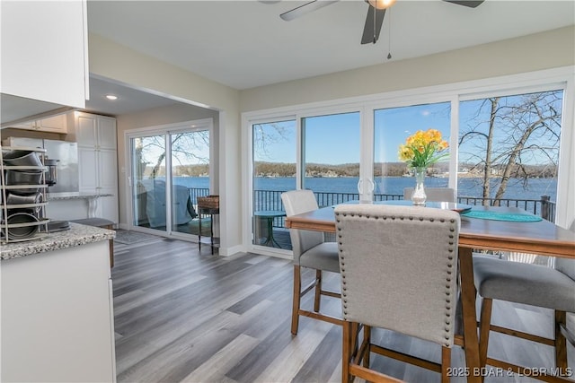 dining space with a water view, light wood finished floors, ceiling fan, and baseboards